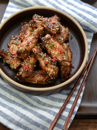 Korean honey garlic chicken coated with sticky sauce is plated and served on a white and blue napkin.