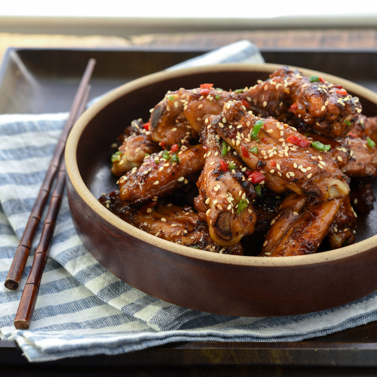 Korean honey garlic chicken is garnished with fresh chilies and served in a bowl on a tray.