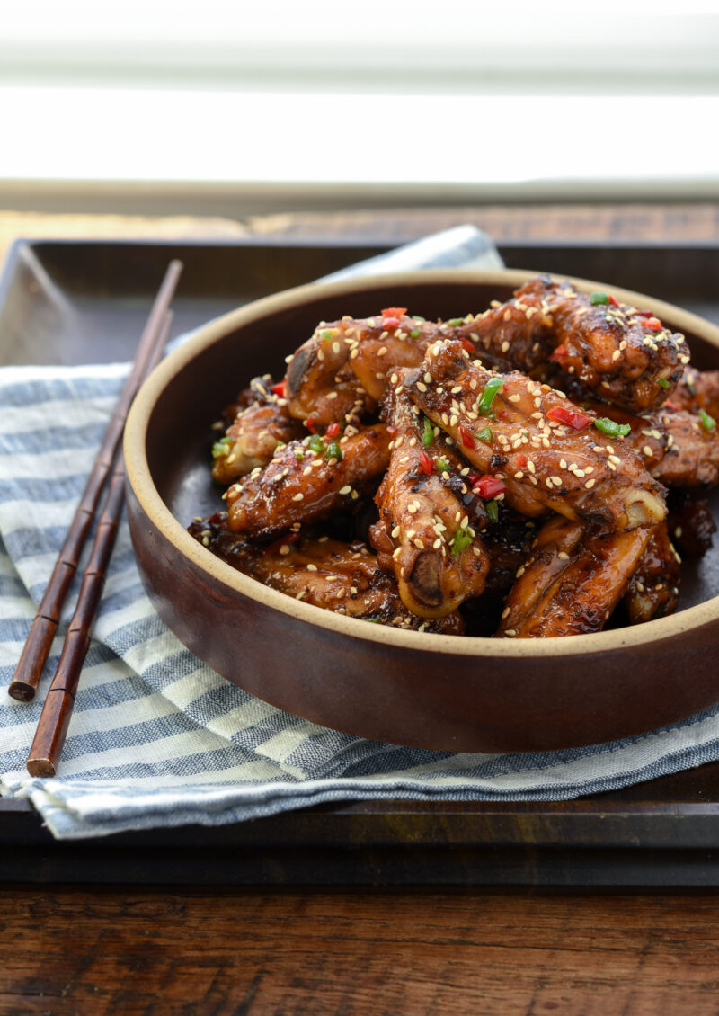 Korean honey garlic chicken is garnished with fresh chilies and served in a bowl on a tray.