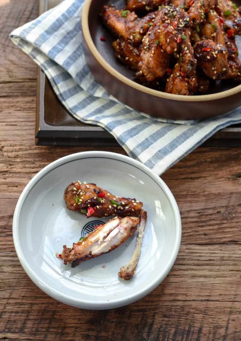 Korean honey garlic chicken wings are garnished with fresh chili and served in a white plate.