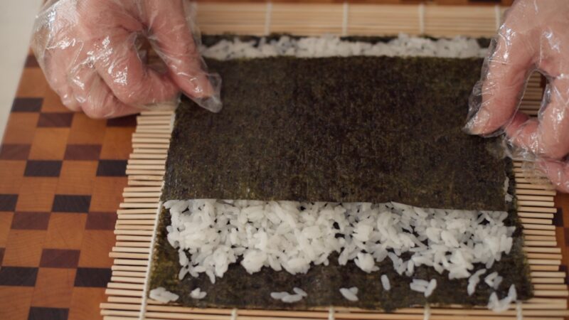 Another layer of seaweed is placed on top of rice over bamboo sushi mat.