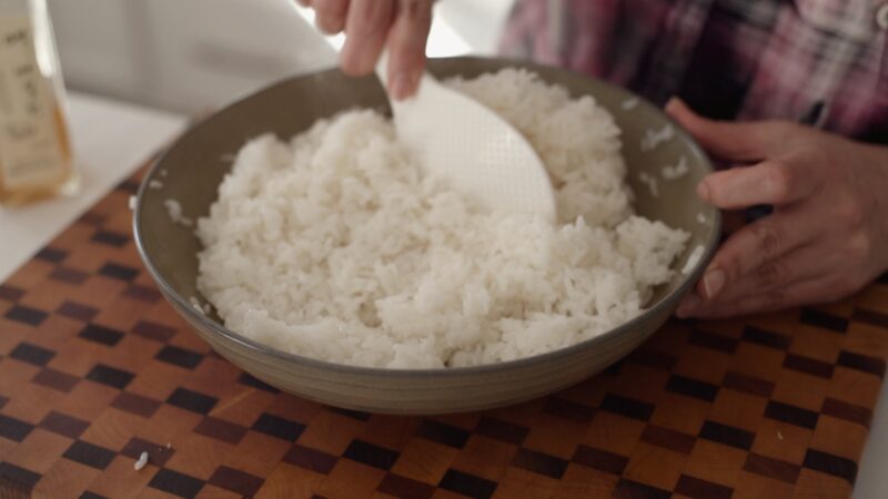 Cooked rice is tossed with Korean plum syrup in a large mixing bowl.