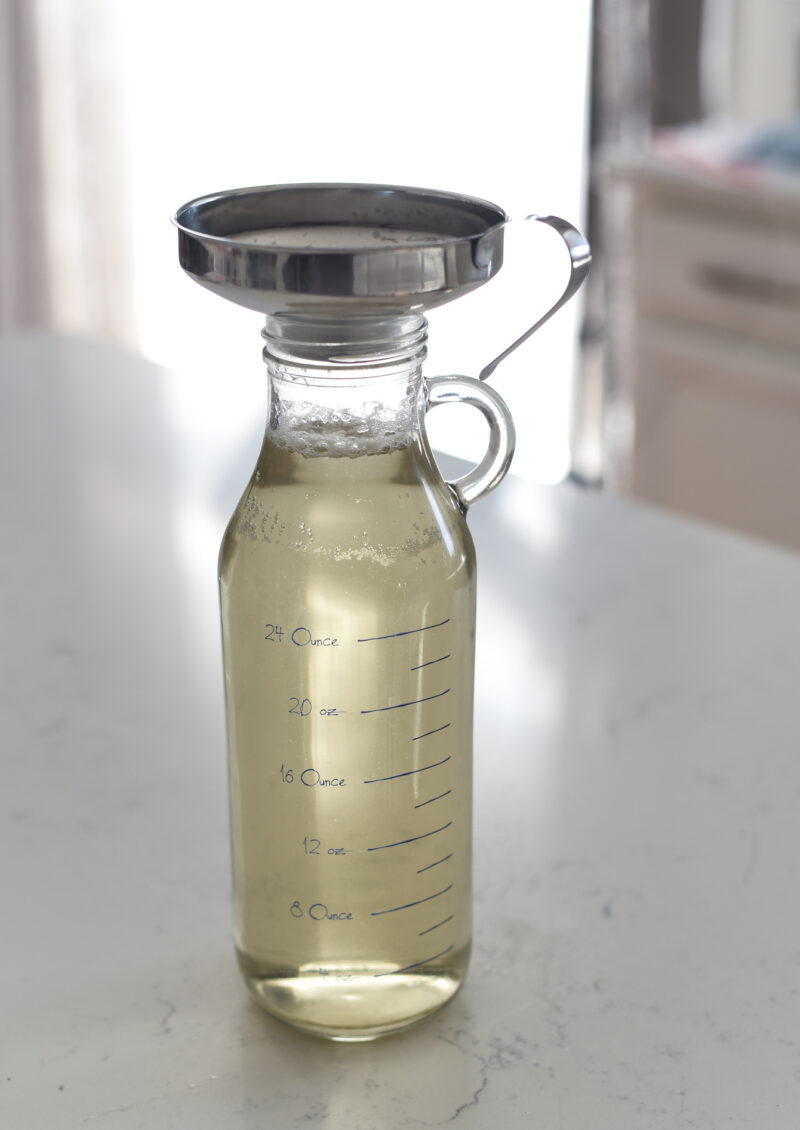 A glass bottle is filled with stock through a kitchen funnel on top.