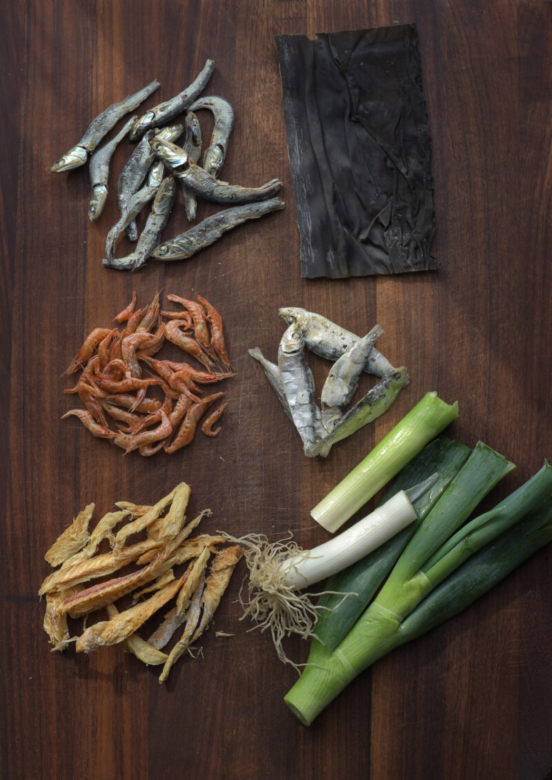 Various dried seafood and leek are displayed on a wooden board.