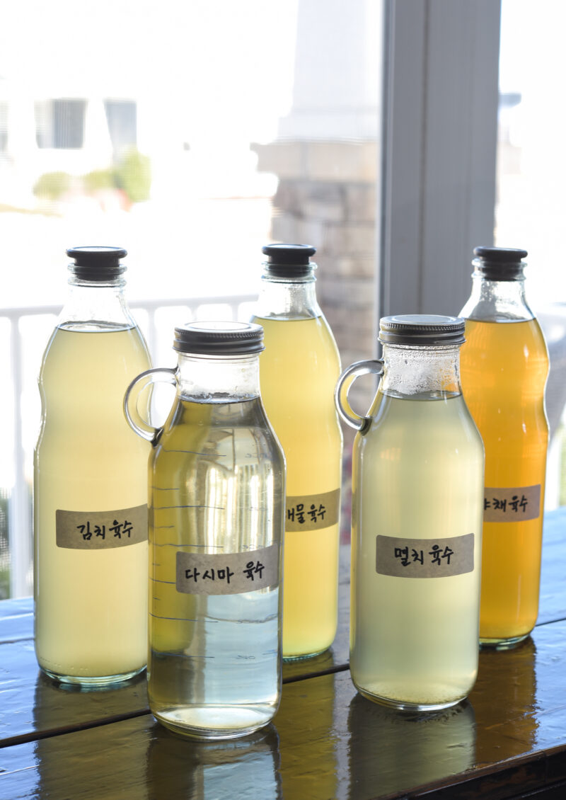 Bottles of various Korean soup stocks with their labels are placed on a counter.