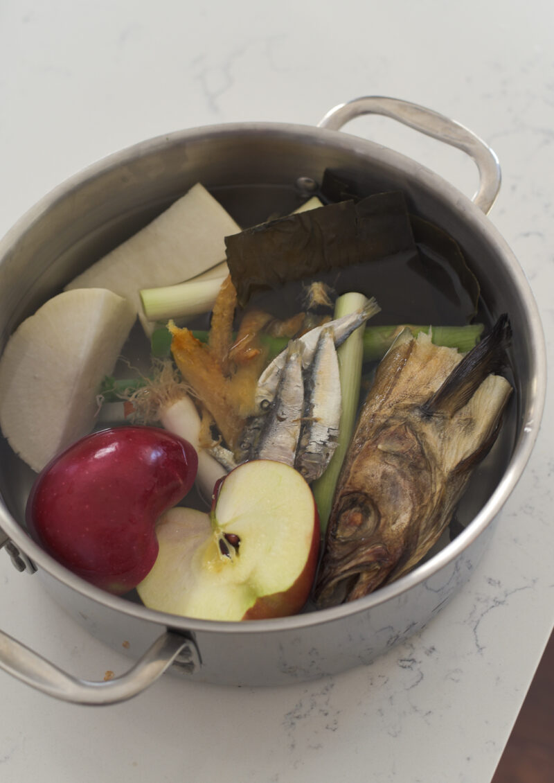 A big pot is filled with dried fish head, apple, radish, and other dried seafood in water.