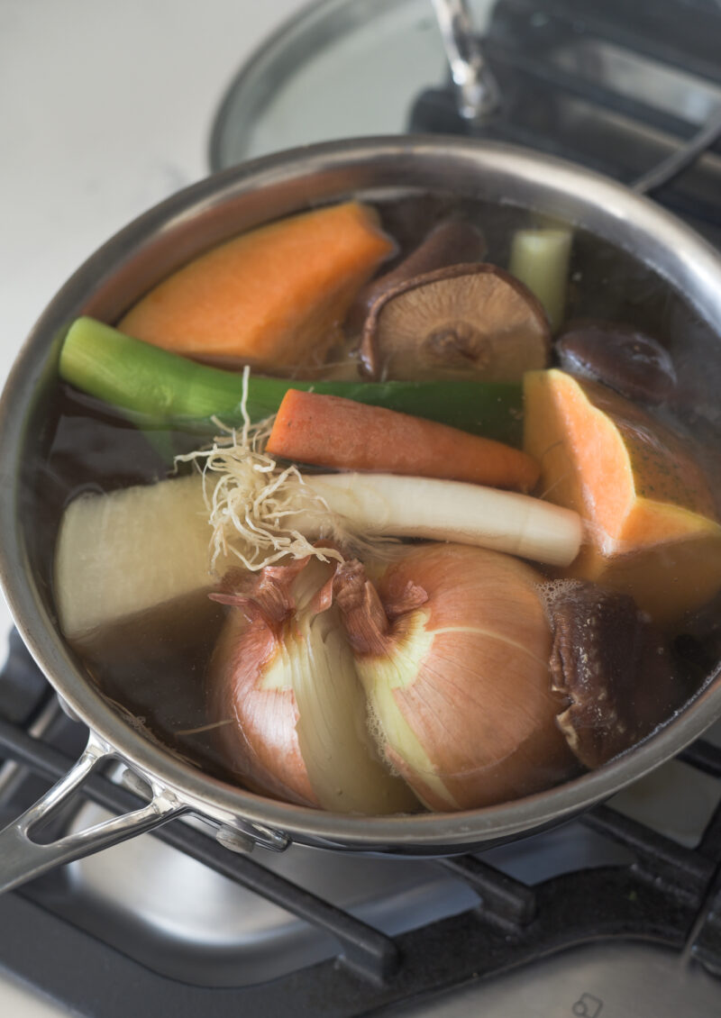 A pot of vegetable stock is simmering with various vegetables and mushroom.