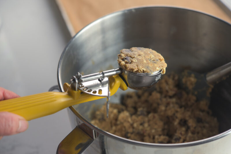 A yellow cookie scoop is holding wheat germ chocolate chip cookie dough.