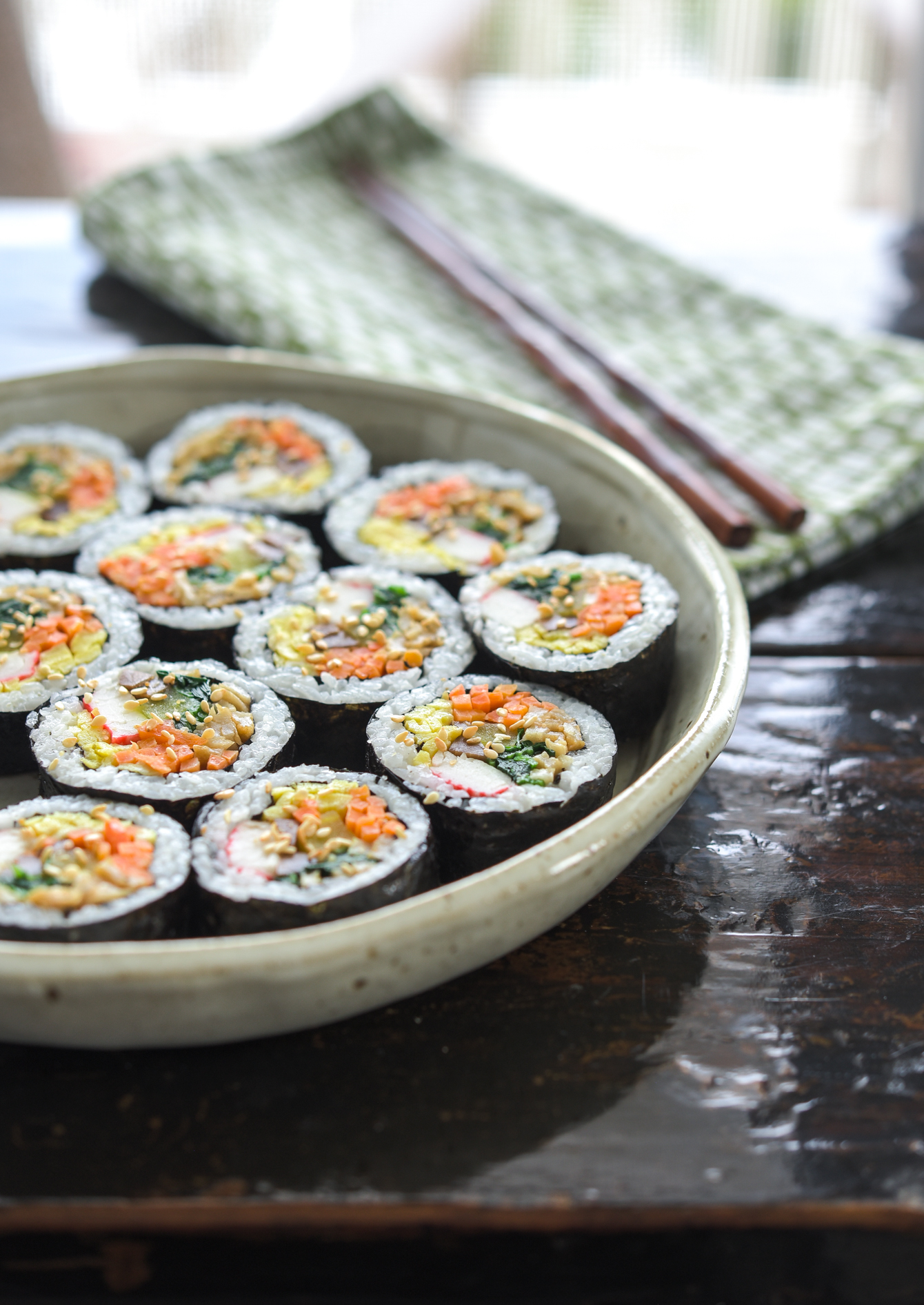 Kimbap pieces are garnished with toasted sesame seeds and placed in a serving dish.