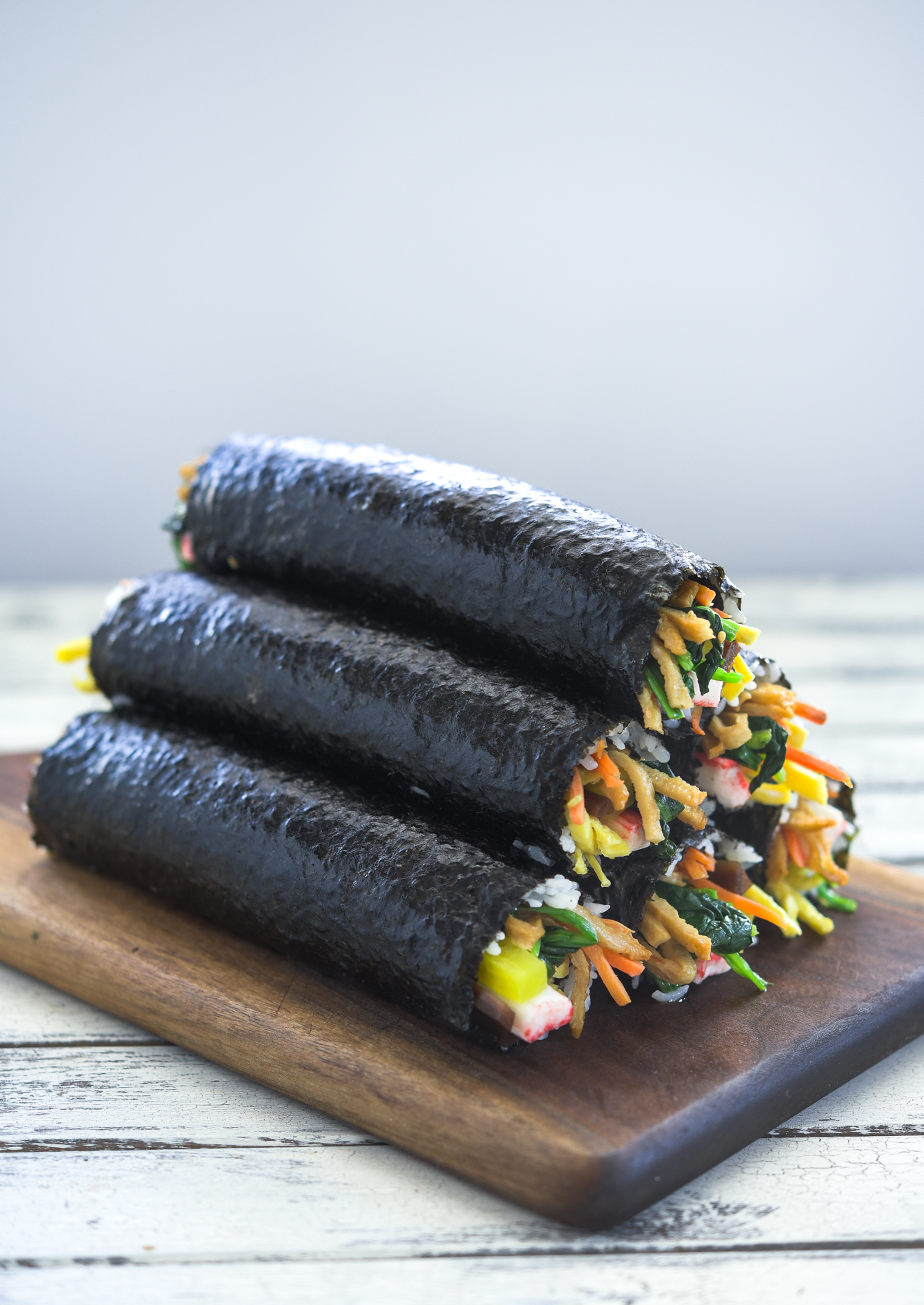 Several kimbap rolls stacked together on a wooden board.
