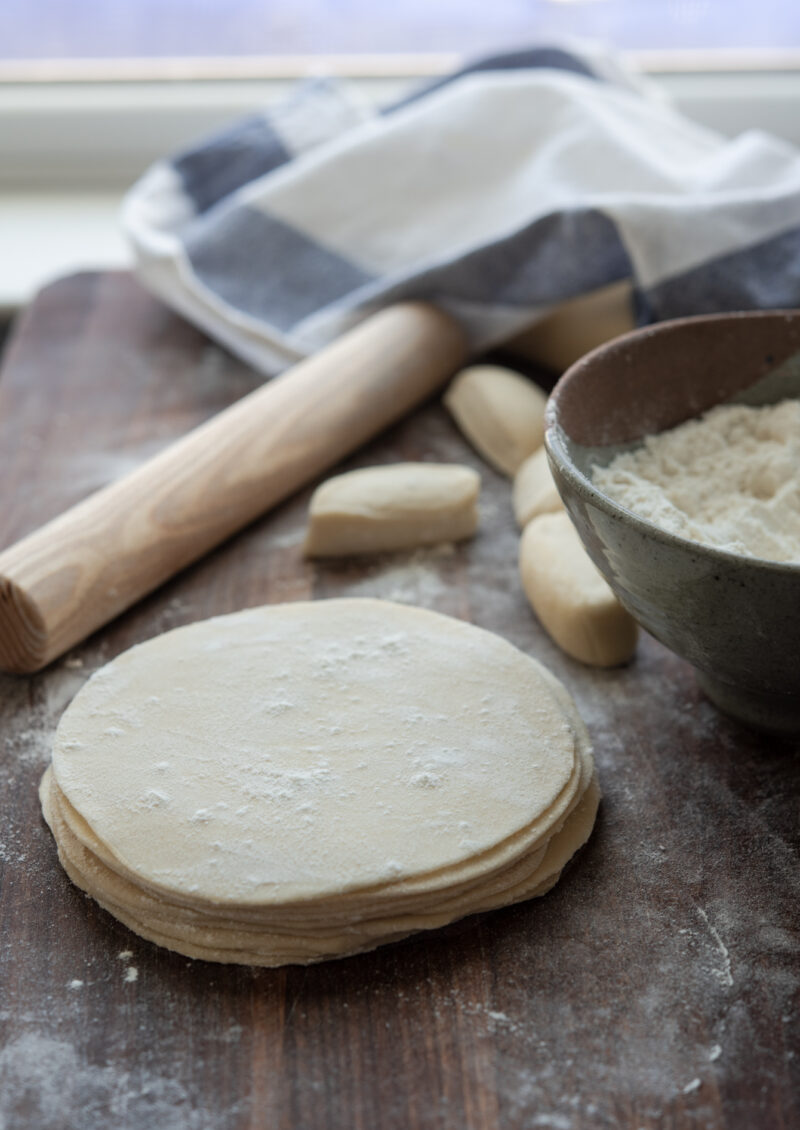 Homemade dumpling wrappers are rolled into circle with a small rolling pin.