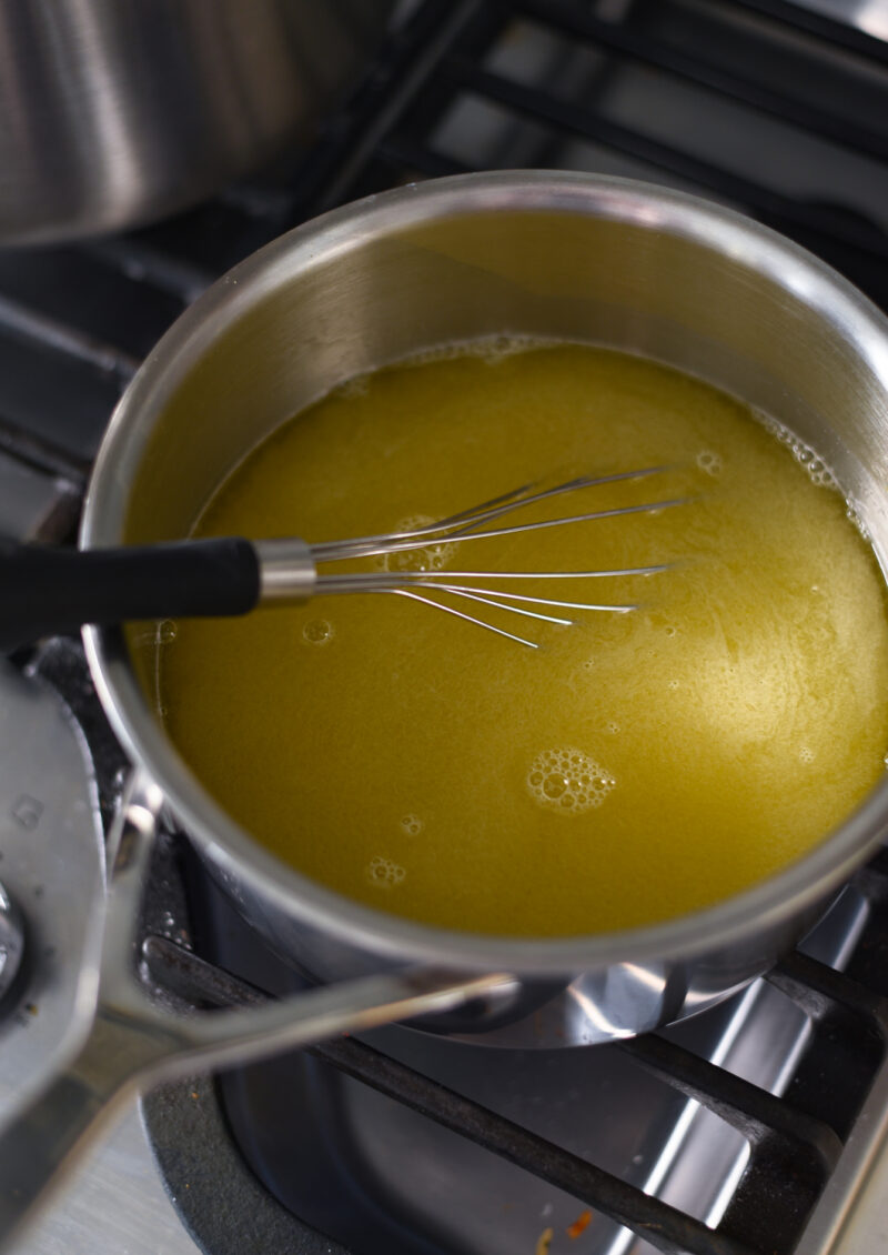 Lemon juice an sugar are combined and simmering in a pot with a flat whisk.