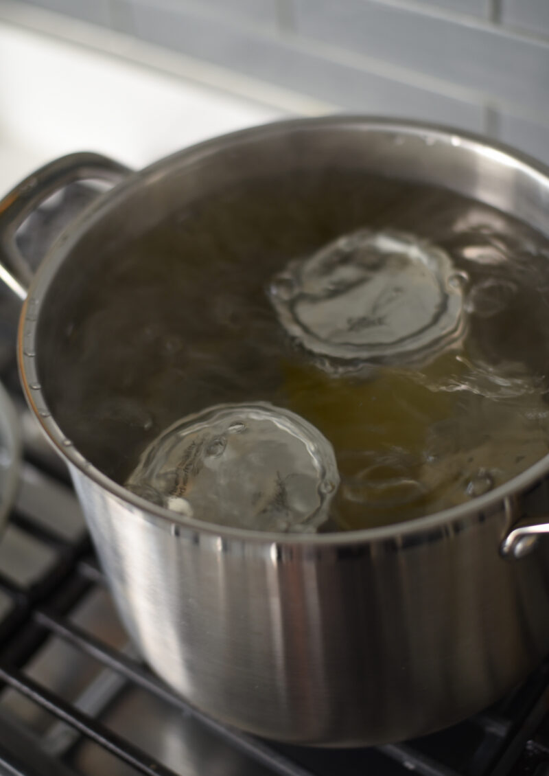 2 jars of lemon syrup sealed with lids are simmering in a boiling water.
