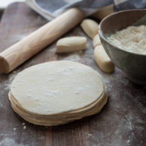 Homemade dumpling wrappers are rolled into circle with a small rolling pin.