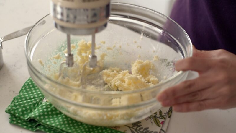 An electric hand mixer is beating butter and sugar in a bowl.
