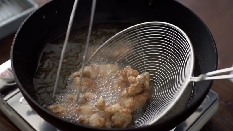 Korean chicken nugget pieces are deep-fried and getting ready to go through skimmer.