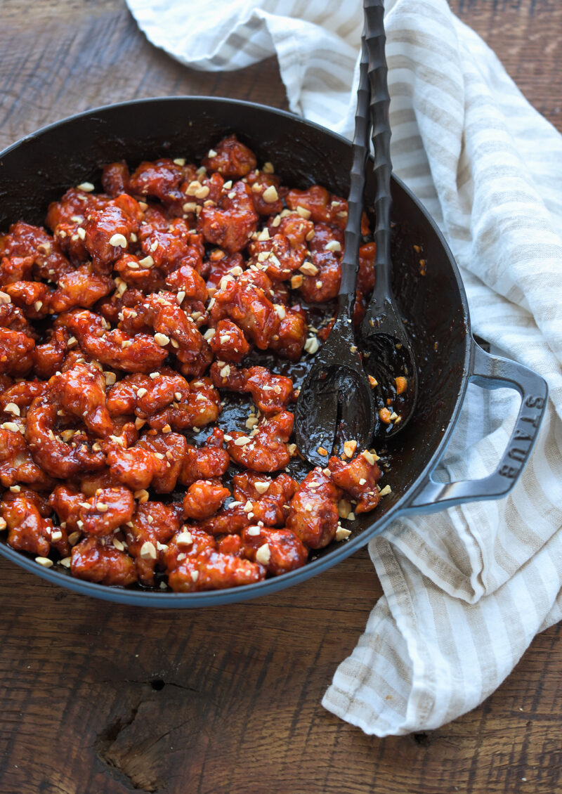 Crispy Korean chicken nuggets are tossed in a sticky glaze with a pair of spoon.