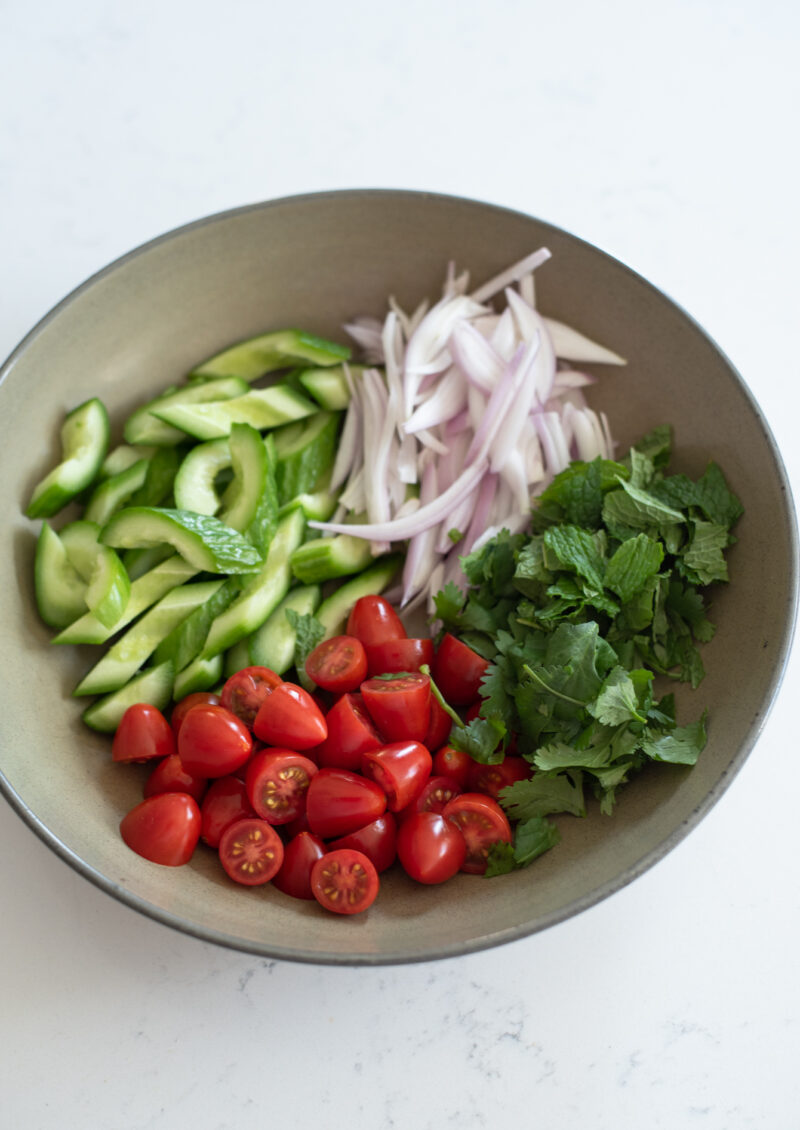 Cucumber, tomato, onion, and mint herb are combined in a bowl.