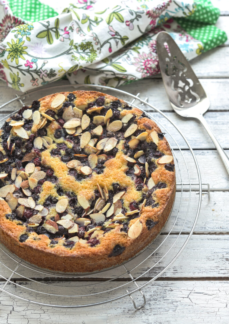 This easy blueberry cake topped with almond slices is cooling on a wired rack.