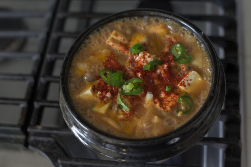 Korean chili flakes and green chilies are added to the boiling soybean paste stew.