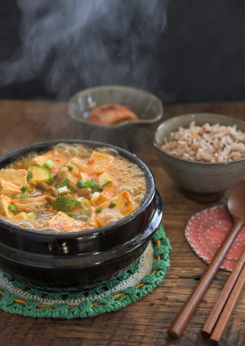 Hot boiling doenjang jjigae in a stone pot is a served with rice and kimchi.