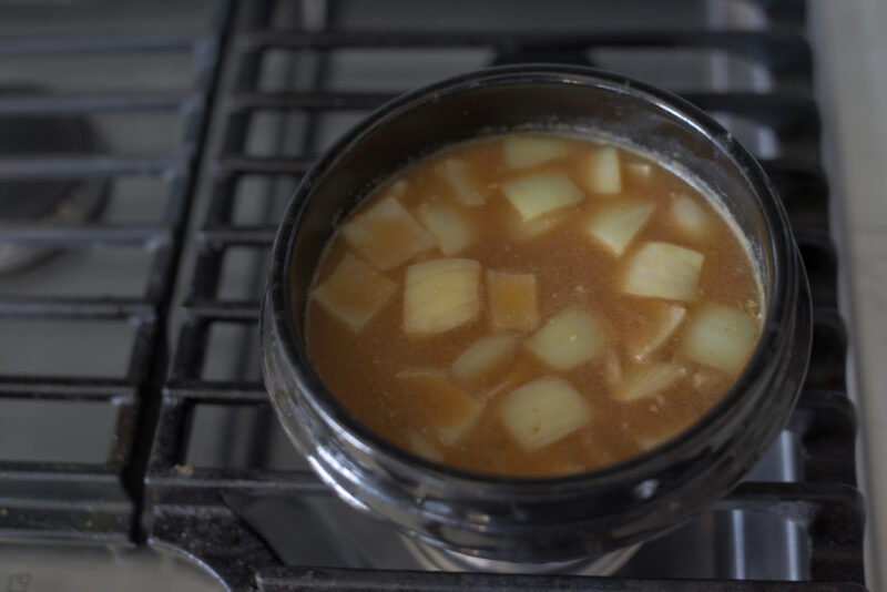 diced onion is added to doenjang jjigae stock in a stone pot.