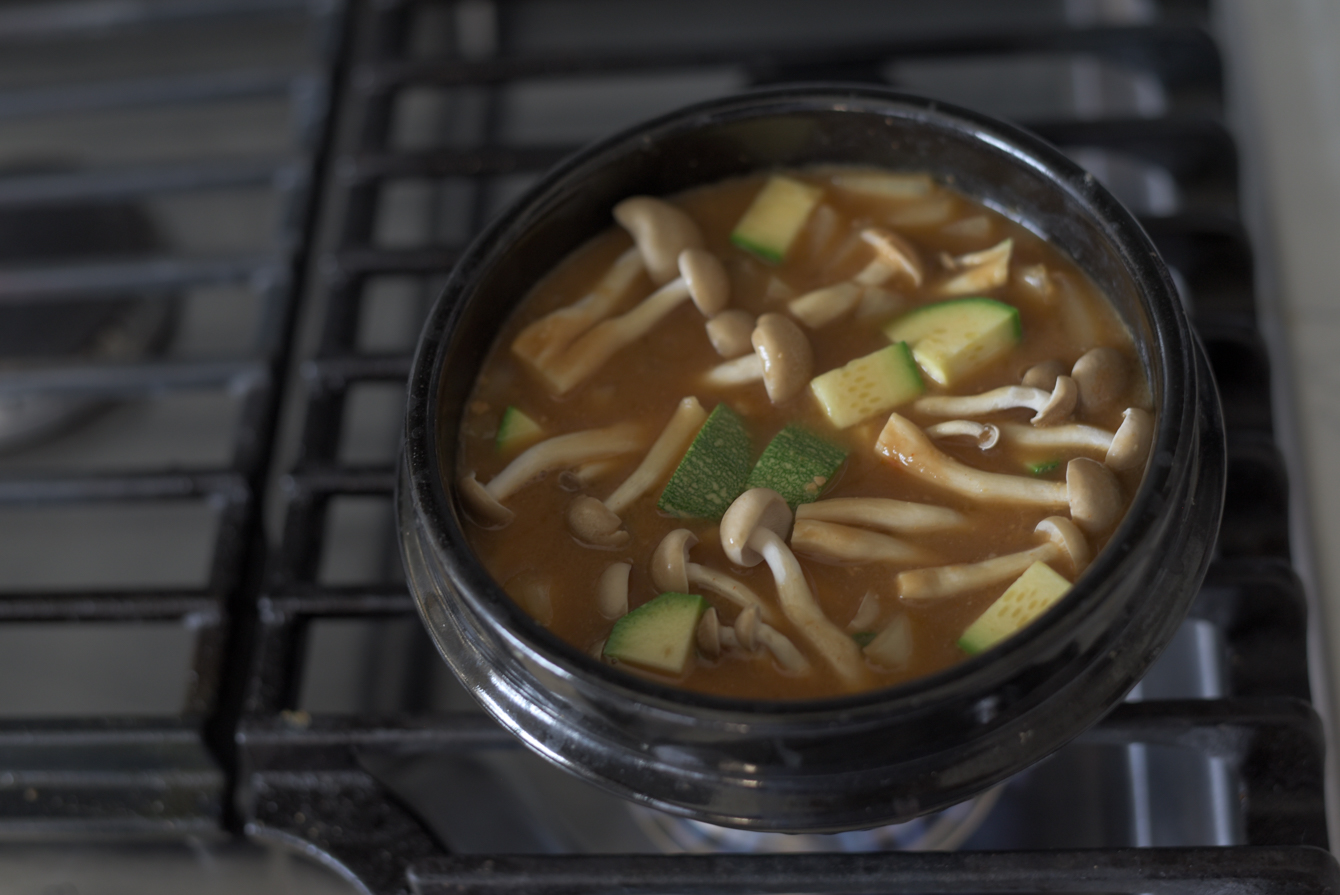 Sliced zucchini and mushrooms added to doenjang jjigae in a pot