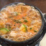 bubbling doenjang jjigae with tofu and zucchini in a hot stone pot