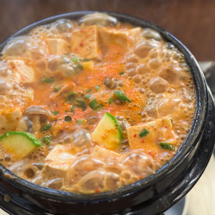 bubbling doenjang jjigae with tofu and zucchini in a hot stone pot