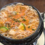 Close-up of bubbling authentic Doenjang Jjigae in a Korean stone pot showing chunks of tofu and zucchini.