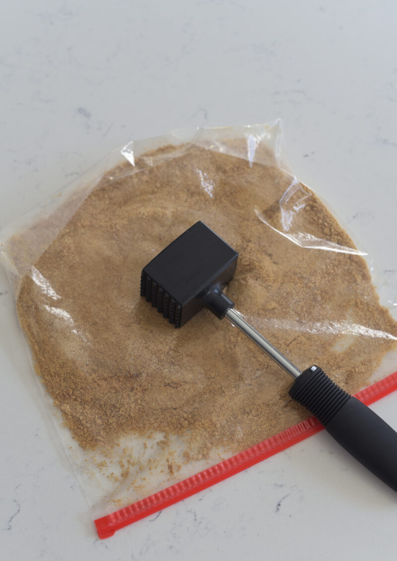A meat hammer is crushing graham cookie crackers in a zip bag.