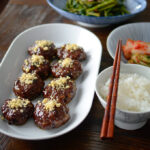 Honey glazed Korean beef patties are garnished with minced pine nuts are served with rice and kimchi on the side.