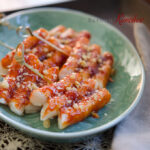 Rice Cakes are on skewers and glazed with sauce made with Korean chili paste (gochujang).