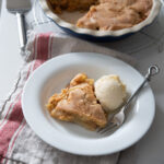 A piece of apple pie is cutout from pie dish and served with vanilla ice cream.