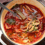 Korean spicy chicken soup (dakgaejang) with vegetables is showing its devilish red look in a white pot.