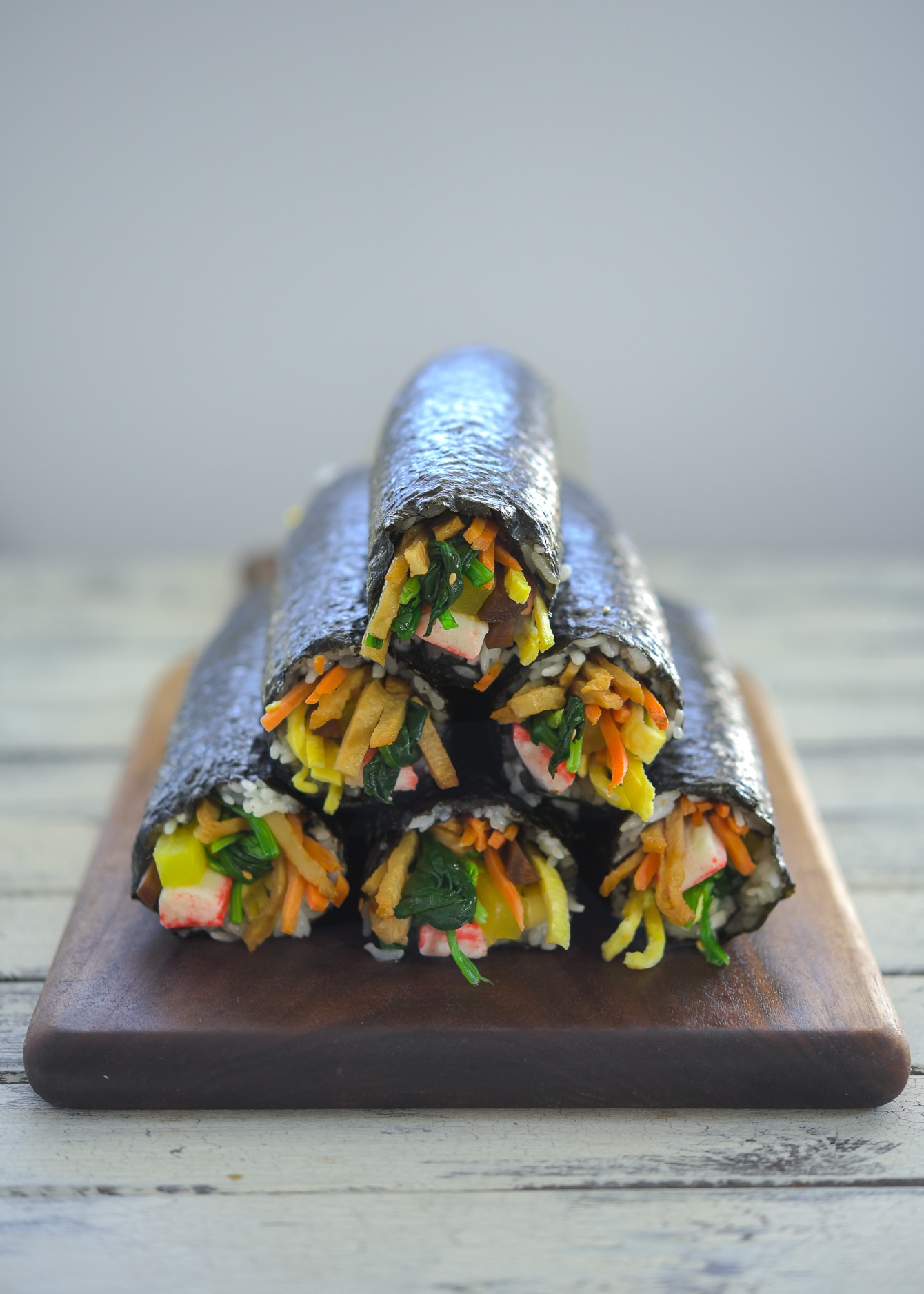 Kimbap (Korean seaweed rice rolls) stacked together on a wooden board.