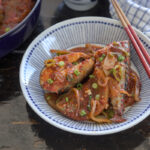 Fresh mackerel fish and radish braised in Korean style chili sauce os served in a dish with chopsticks.