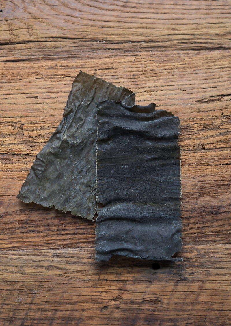 Two pieces of dried sea kelp are placed on a wooden board.