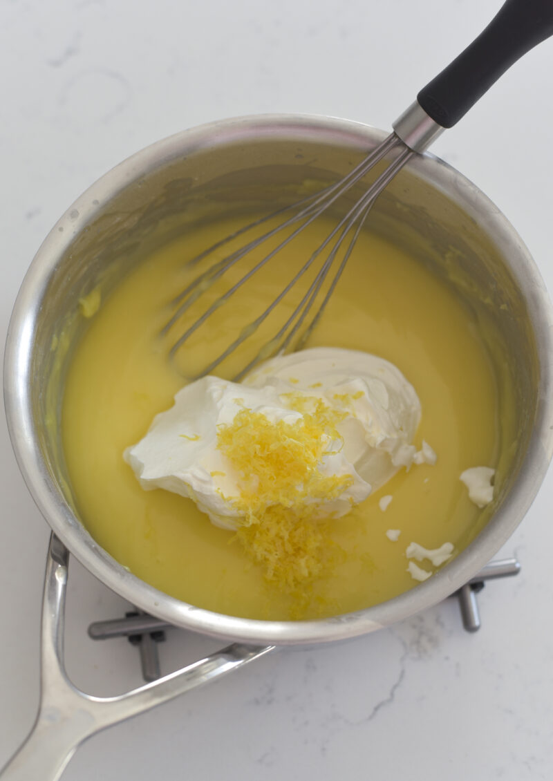Sour cream and lemon zest are added to a lemon custard in a pan on a cooling rack.