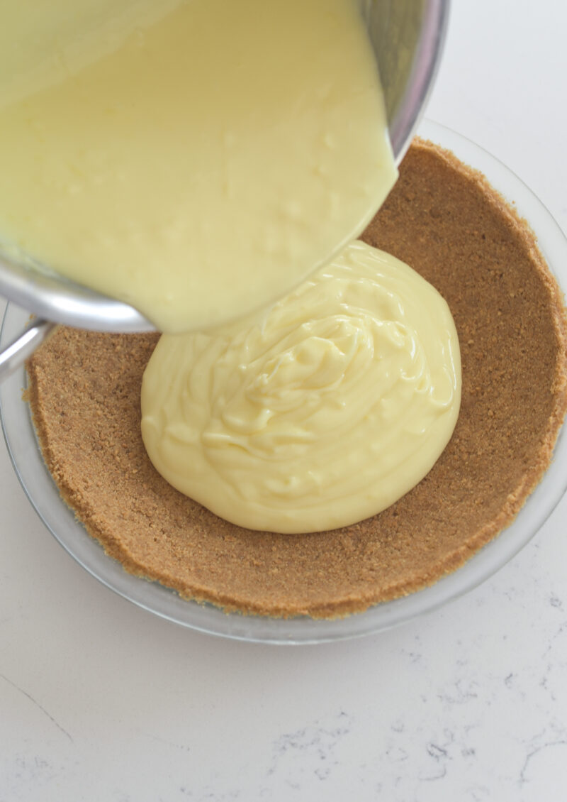 Lemon custard is being poured onto a prepared graham cookie pie crust.