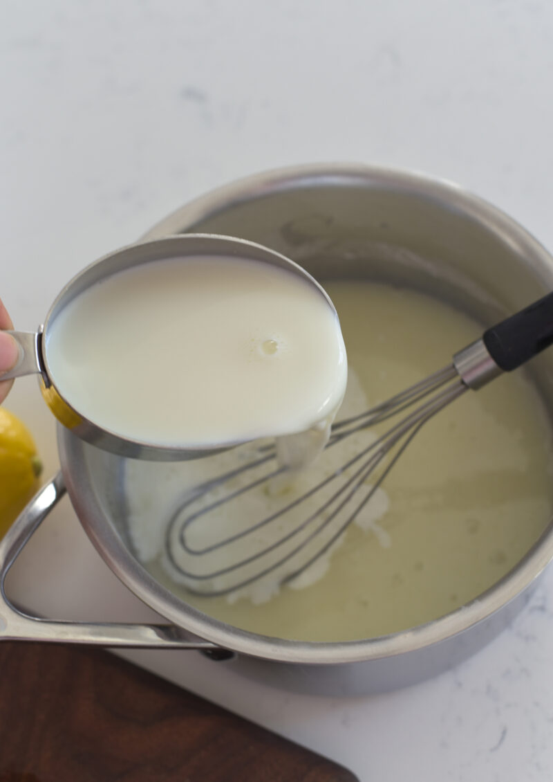 A cup of milk is added to lemon and sugar mixture in a pan.