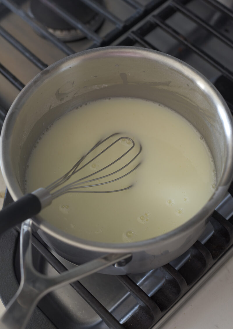 A flat whisk is stirring the lemon sugar mixture in a pan on the stove.