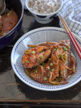 Fresh mackerel fish and radish braised in Korean style chili sauce os served in a dish with chopsticks.