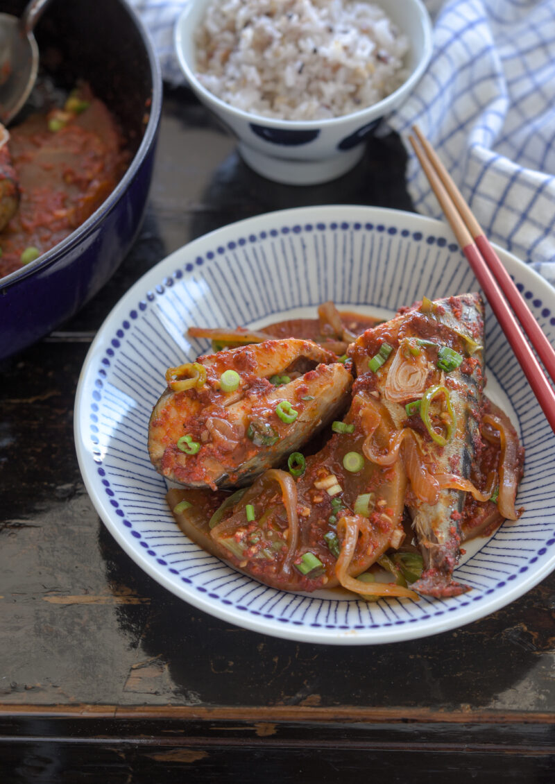 Fresh mackerel fish and radish braised in Korean style chili sauce os served in a dish with chopsticks.