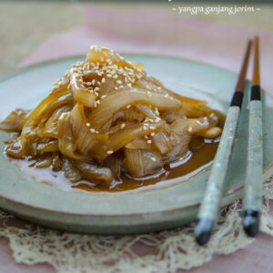 Soy braised onion side dish is served on a green plate with chopsticks.