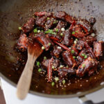 Chinese Sweet and Sour Pork Ribs are coated with sticky caramelized sauce and garnished with green onion.