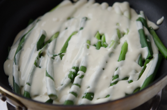 Pancake batter is drizzled over scallions in a skillet.