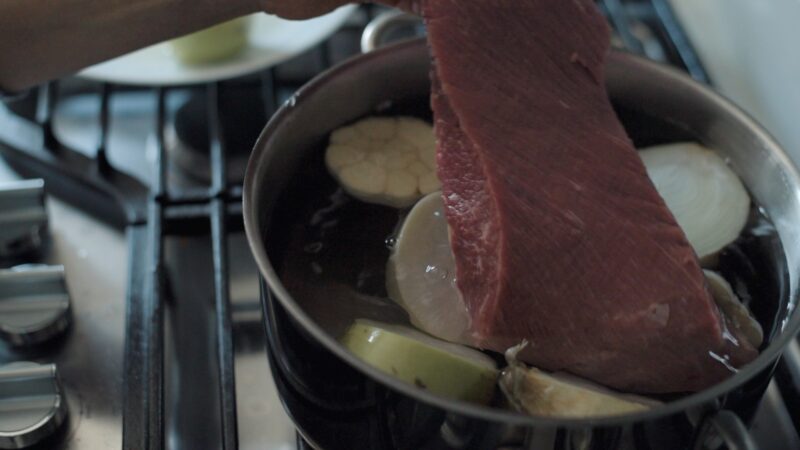 A chunk of beef brisket is added to onion, radish in pot of water to make beef stock.