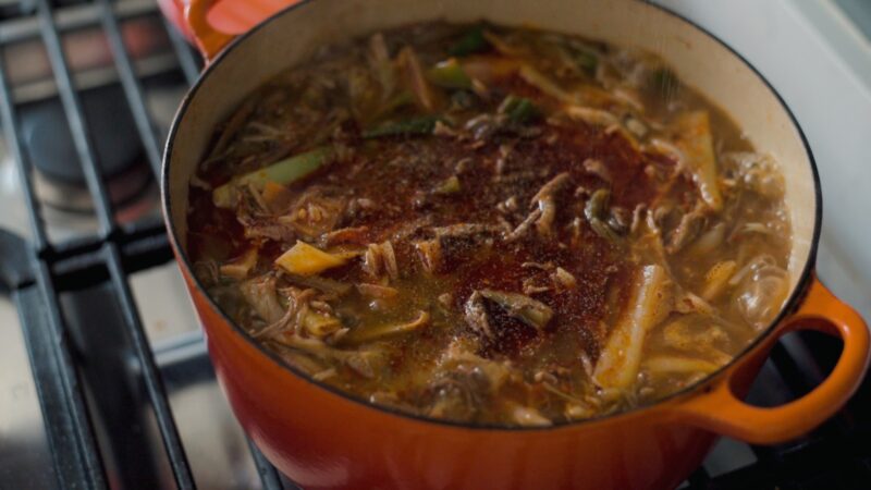 A pot of simmering spicy Korean beef soup is on the stove and seasoned with black pepper.