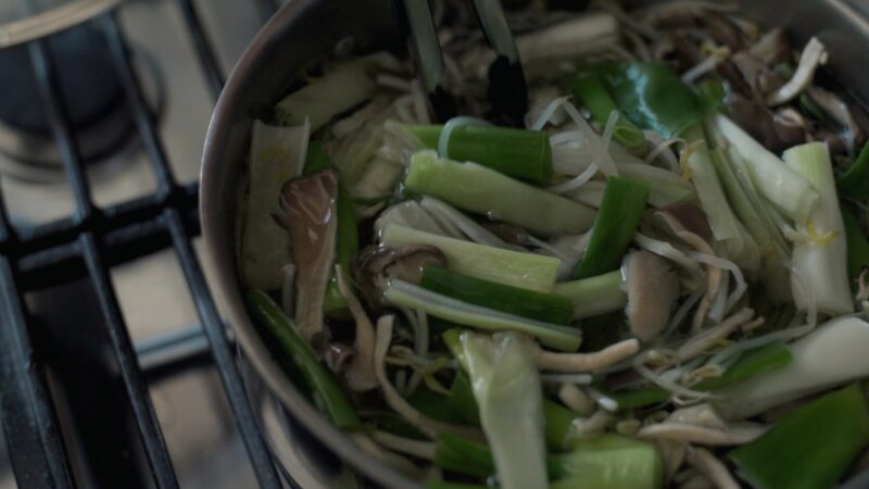 Mushrooms and leek slices are added to blanch in a pot.